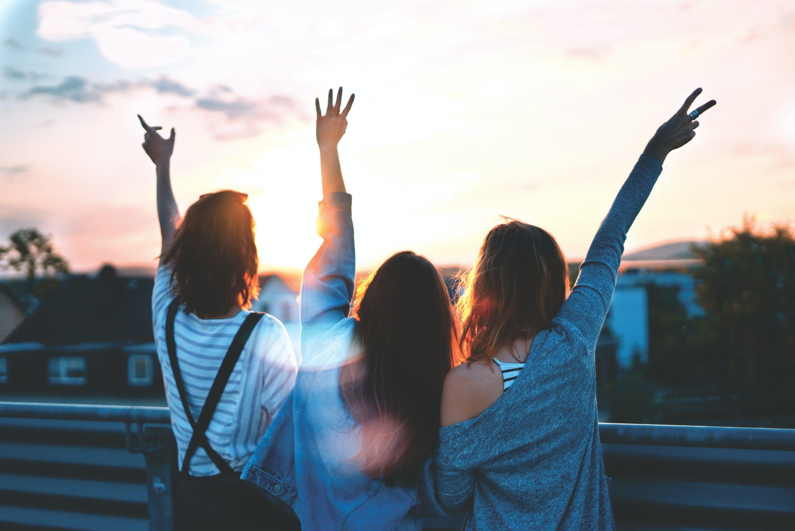 Vier Freundinnen werfen fröhlich ihre Hände in die Luft, symbolisierend die Freude und Verbundenheit in einer gesunden Freundschaft.